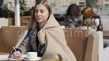年轻的白种人妇女在露台上的桌子旁坐着，一边用毯子盖着工作。 那个女孩在她身上<strong>扭动</strong>